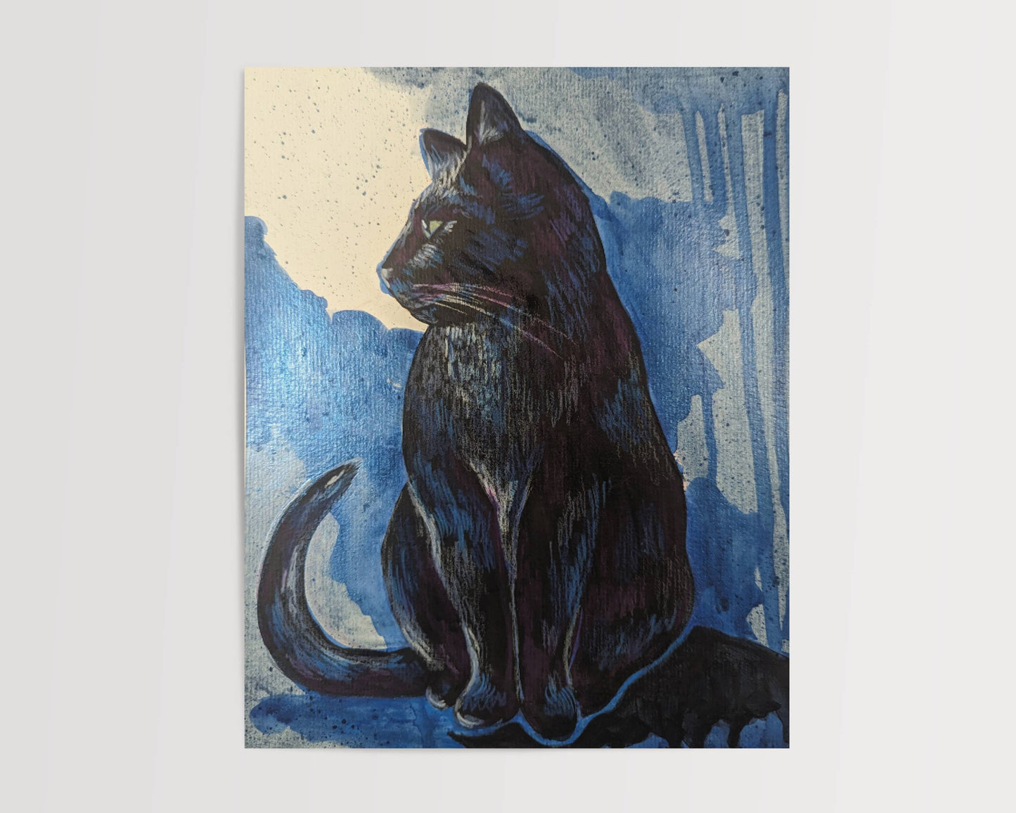 A framed black cat art print sitting on a woven rattan shelf with sunlight casting shadows on the wall