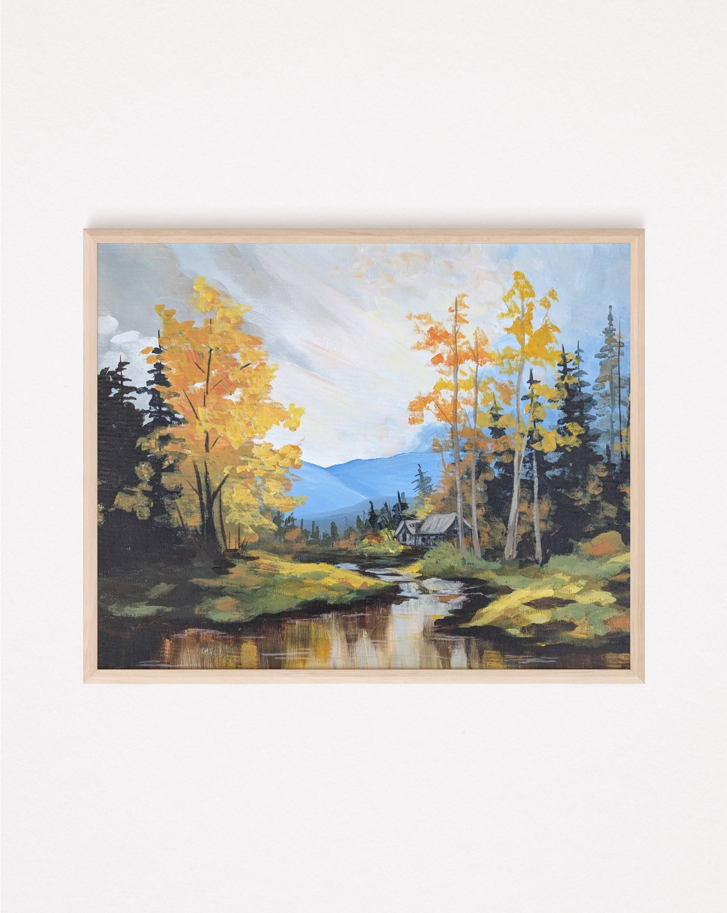 A framed art print of an autumn landscape with vibrant golden-yellow trees by a river with distant mountains in the background under a cloudy sky