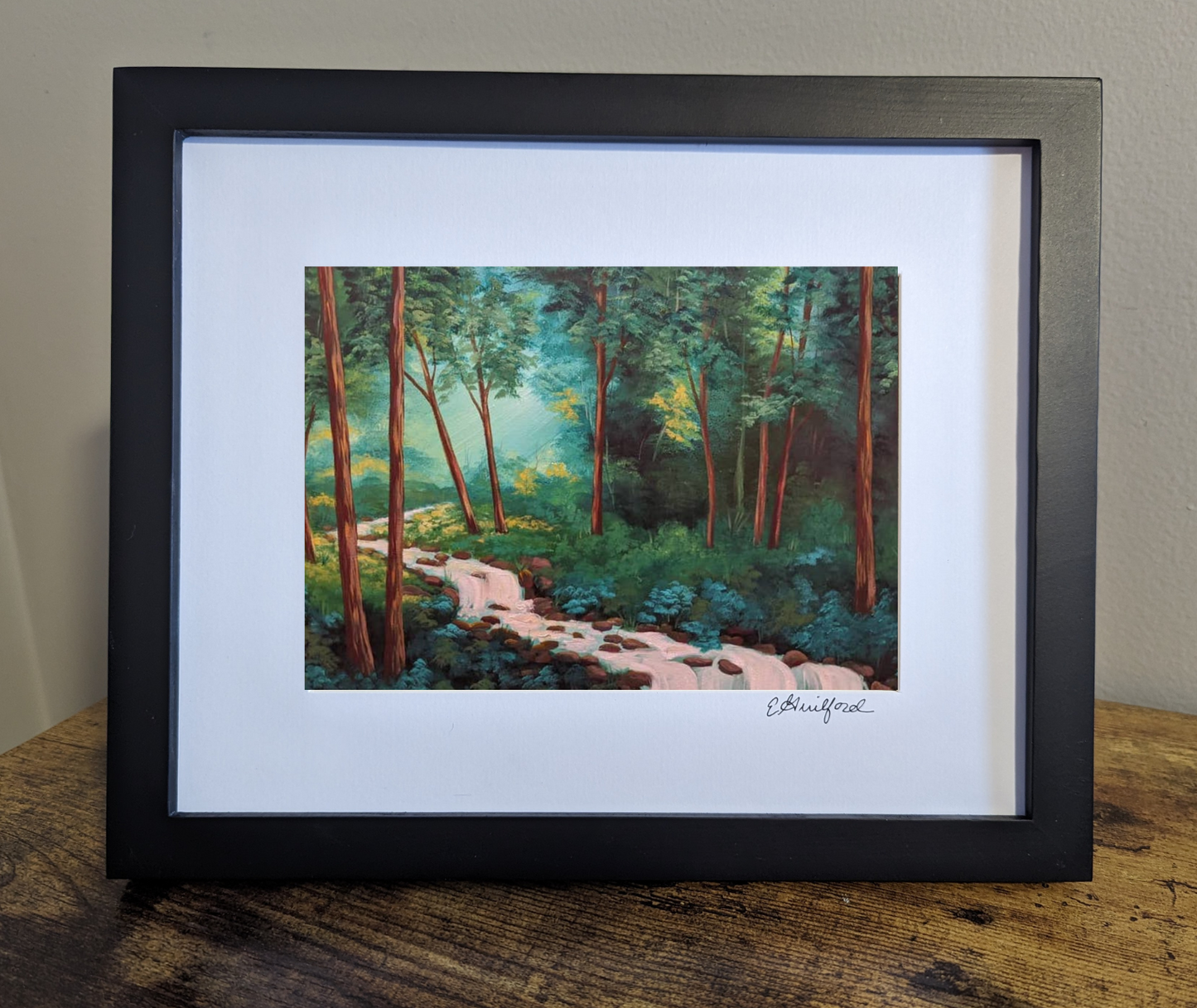 Framed art print depicting rays of sunshine coming through a lush green forest with a gently flowing stream running through