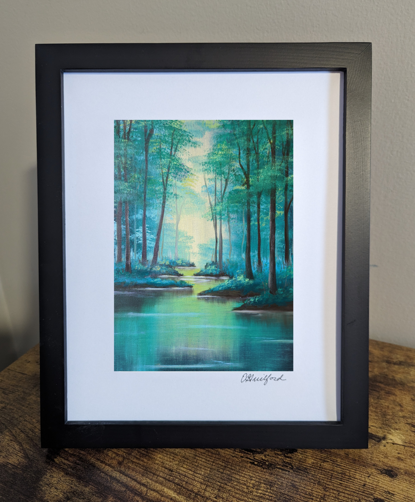 A tranquil framed art print depicting tall trees alongside a calm river illuminated by soft sunlight filtering through the trees