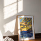 A framed sunset art print named Harmony leaning against a wall on a wooden floor