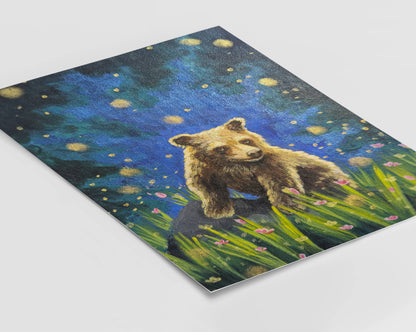 Art print of a brown bear cub sitting in a meadow filled with pink flowers in summer under a glowing sky with fireflies