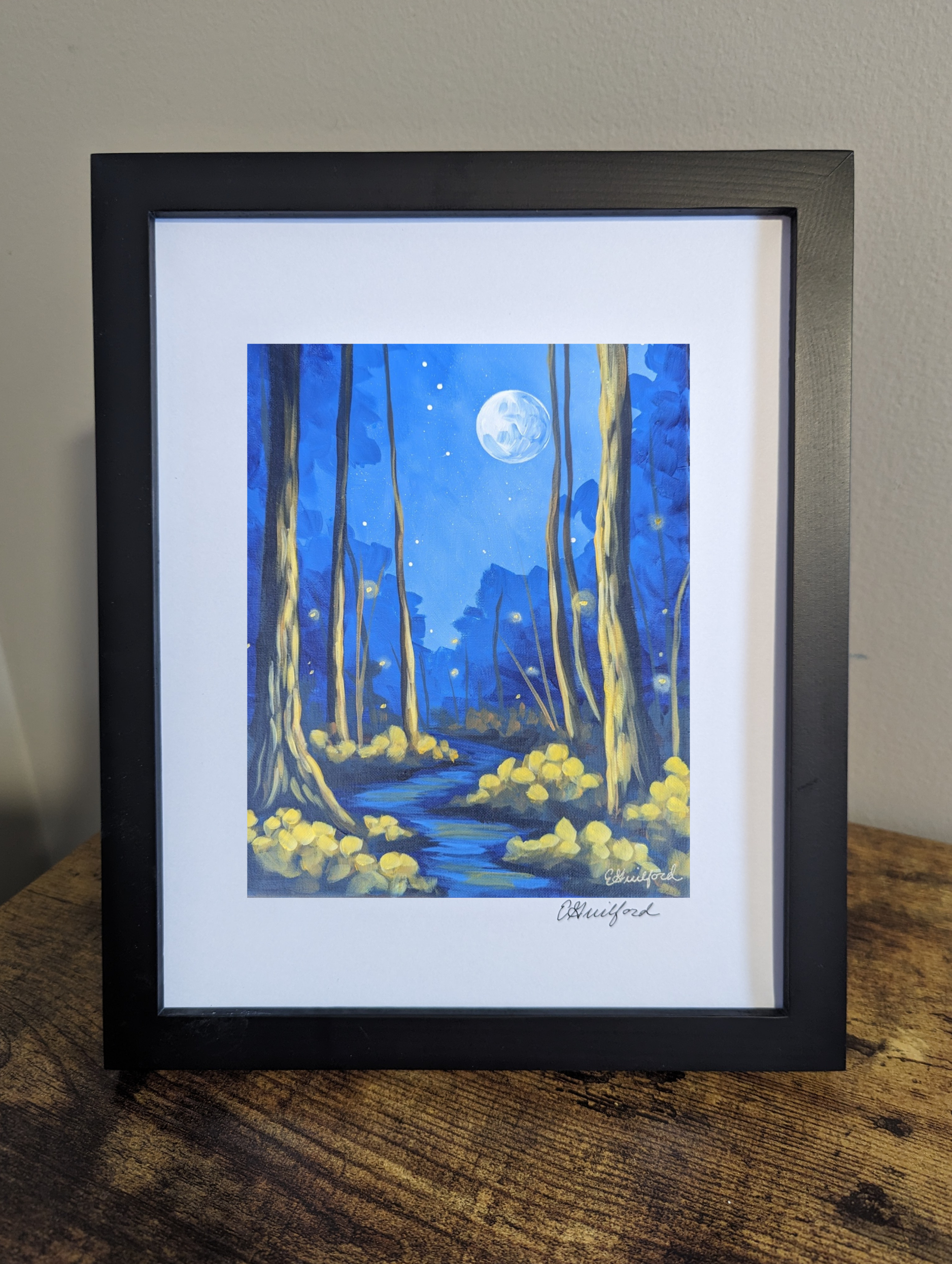 A framed art print of a moonlit dark forest full of fireflies featuring a full moon and trees