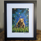 Art print of a brown bear cub sitting in a meadow filled with pink flowers in summer under a glowing sky with fireflies