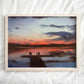 Art print of tranquil sunset scene over a small lake with two chairs placed at the end of a dock